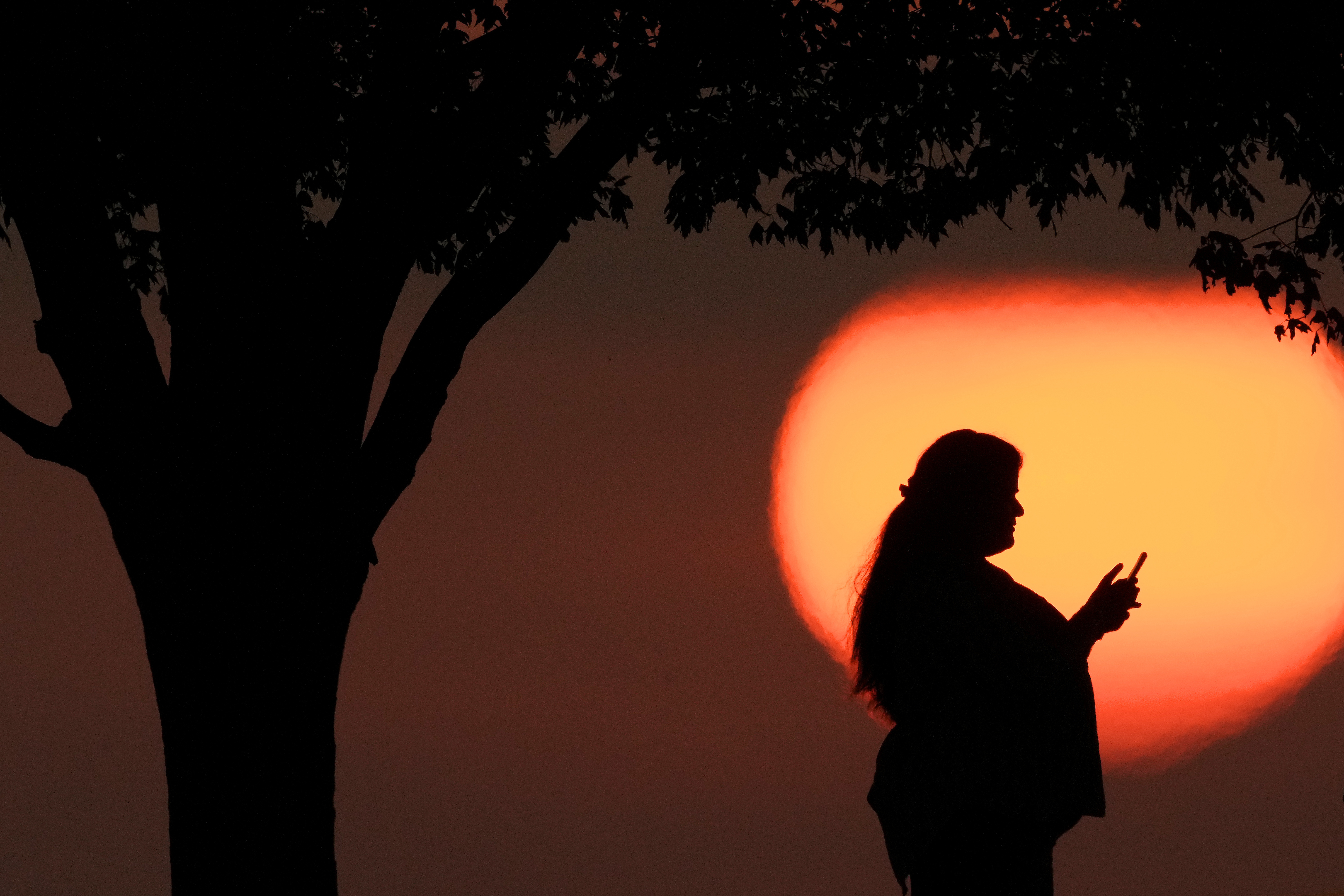 A woman looks at her phone while watching the sun set in Kansas City, Mo.